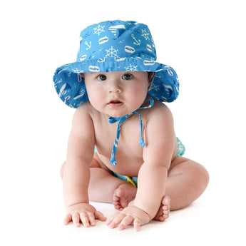 A baby wears Bumkins Sun Hat: Ahoy, a blue, nautical print hat with adjustable drawstring and UPF 50+ protection on a white background.