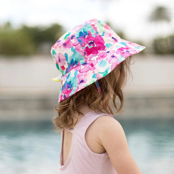 Child in a Bumkins Sun Hat: Watercolor and pink swimsuit with drawstring, by the pool; made from UPF 50+ fabric for sun protection.