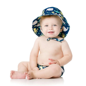 Bumkins baby in a Deep Sea sun hat with drawstring and marine animal diaper, sitting on a white background.