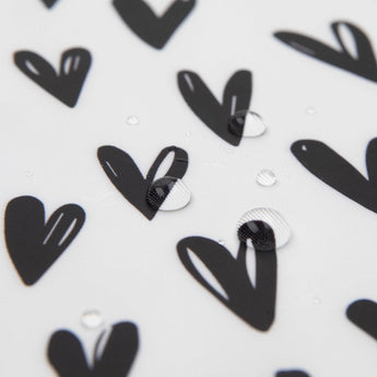 Close-up of black hearts on Bumkins Sleeved Bib glistening with water droplets on the white fabric.