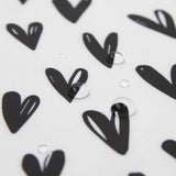 Close-up of water droplets on Bumkins Junior Bib: Hearts, featuring black heart shapes on stain-resistant fabric.