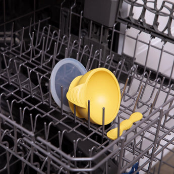 A Bumkins Silicone First Feeding Set in Pineapple, featuring a yellow helmet and suction bowl, fits snugly in the dishwasher.