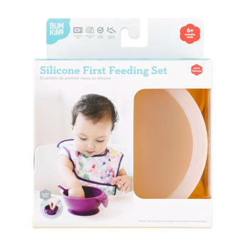 A baby explores self-feeding with Bumkins Silicone First Feeding Set: Pineapple, featuring a suction bowl and spoon in purple.