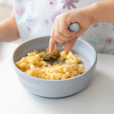 Close-up of a child enjoying mac and cheese from Bumkins Silicone Grip Bowl: Gray using a spoon at a white table.