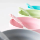 Close-up of four bowls and spoons, including Bumkins Silicone Grip Bowl: Pink, on a white background.