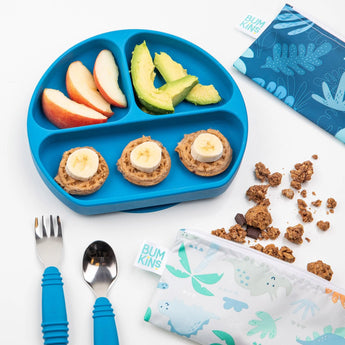 The Bumkins Silicone Grip Dish in Dark Blue is ideal for toddler meals like apple slices, avocado, and waffle pieces, with pouches and utensils handy.