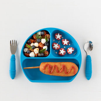 Bumkins Silicone Grip Dish: Dark Blue holds a salad, star-shaped fruit, and a corn dog with toddler portions. A fork and spoon are beside it.