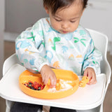 A toddler in a high chair enjoys yogurt and fruit on a Bumkins Silicone Grip Dish: Tangerine, using its suction base for mess-free meals.