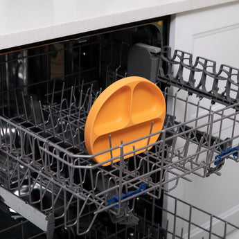 The Bumkins Silicone Grip Dish in Tangerine is upright in the bottom rack of an open dishwasher.