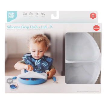 A child uses a marble Silicone Grip Dish with Lid by Bumkins, wearing a bib, while the packaging displays the Bumkins branding.