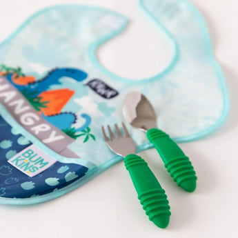 Close-up of a spoon and fork set and dinosaur-themed bib from Bumkins Ultimate Gift Set - Dinosaurs & Blue Tropic on a white background.