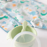 Close-up of a dinosaur-themed bib and bowl with spoon and lid from Bumkins Ultimate Gift Set - Dinosaurs & Blue Tropic on a white background.