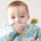 A baby in a dinosaur-print bib from Bumkins Ultimate Gift Set - Dinosaurs & Blue Tropic in a bright room.