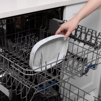 A hand places a Bumkins Silicone Grip Tray: Marble into the top rack of an open dishwasher.