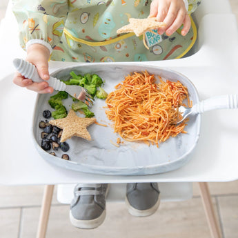 A child in a high chair enjoys pasta, broccoli, and blueberries from a Bumkins Silicone Grip Tray: Marble with a fork.
