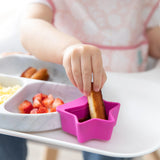 Close-up of a child dipping French toast in a fuchsia Bumkins Silicone Little Dipper 3-Pack: Lollipop, attached to a plate on a high chair.