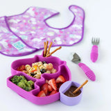 A unicorn-shaped plate with food, a purple Bumkins Silicone Little Dipper 3-Pack: Lollipop, utensils, and a bib on a white background.