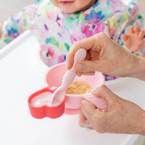 An adult uses spoon to feed a baby in a high chair from a red Bumkins Silicone Little Dipper 3-Pack: Tutti-Frutti.