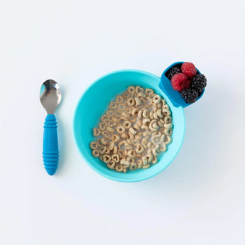 A blue cereal bowl with blue Bumkins Silicone Little Dipper Round 3-Pack: Gumdrop with berries sits next to a spoon on a white background.
