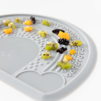 Close-up of Bumkins Silicone Sensory Placemat: Gray on a white background, covered in diced fruit.