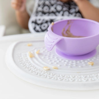Close-up of a purple bowl sitting on a Bumkins Silicone Sensory Placemat: Marble on a white table.
