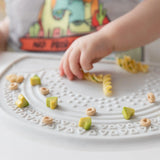 Close-up of a child eating pasta, avocado, and cereal from a Bumkins Silicone Sensory Placemat: Marble.