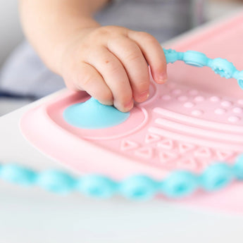 Close-up of a child's hand on a Bumkins Silicone Sensory Placemat: Pink.