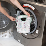 A person loading a floral-patterned SuperBib® from the Bumkins Love You Bunches 3 Pack into a front-loading washer.