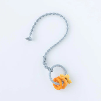 A Bumkins Silicone Accessory Tether 2-Pack: Gray attached to an orange and gray teething toy on a white background.
