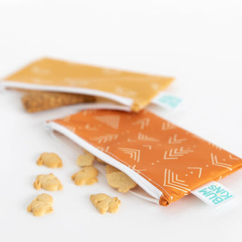 Bumkins Reusable Snack Bag, Small 2-Pack: Sunshine and Grounded lays partially open on a white background with snacks spilling out.