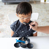 A child happily enjoys yogurt, being fed by an adult with a Bumkins Silicone Dipping Spoons: Mickey Mouse (Black and Blue) from a bowl.