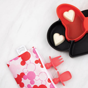 Red Silicone Chewtensils® by Bumkins, heart molds, and a pink Disney pouch with Mickey Mouse on white.