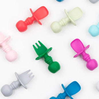Silicone Chewtensils®: Red by Bumkins feature pacifier-like handles and sensory bumps, with forks and spoons arranged on white.