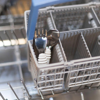 Open dishwasher with cutlery in a utensil basket, featuring Bumkins Spoon + Fork: Gray toddler set.
