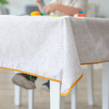 Close-up of a Bumkins Splat Mat: Wander draped over a table, with a child blurred in the background.