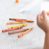 Close-up of a child's hand reaching for crayons on a Bumkins Splat Mat: Wander.