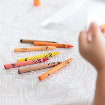 Close-up of a child's hand reaching for crayons on a Bumkins Splat Mat: Wander.