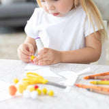 A child crafting with glue, pom-poms, scissors, and crayons on a Bumkins Splat Mat: Wander.