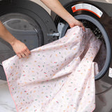 A person places Bumkins Splat Mat: Princess Magic into an open front-loading washing machine.