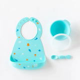 Bumkins Silicone Bib: Ocean Life lays next to a blue bowl, matching spoon, and transparent lid on a white background.