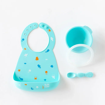 Bumkins Silicone Bib: Ocean Life lays next to a blue bowl, matching spoon, and transparent lid on a white background.