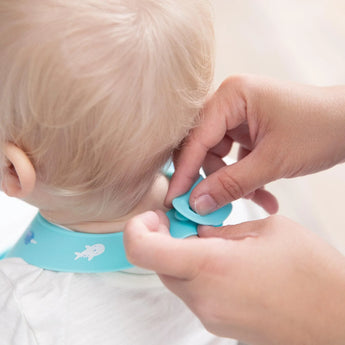 Close-up of hands fastening the closure of a Bumkins Silicone Bib: Ocean Life around a child's neck.