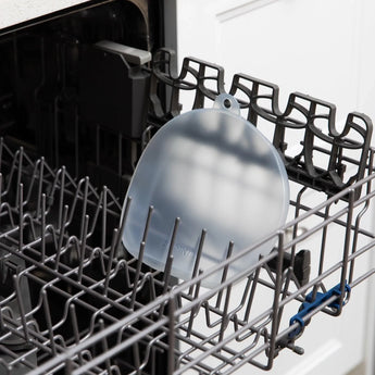 A CPSIA-compliant Grip Dish Silicone Stretch Lid by Bumkins, securely placed in a transparent dishwasher rack.