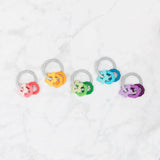 Five teething toys sit on a white marble background, including Bumkins Silicone Teething Charms: Orange.