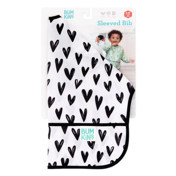 Bumkins Sleeved Bib: Hearts, waterproof with crumb catcher, features black hearts on white and a child in a green shirt.