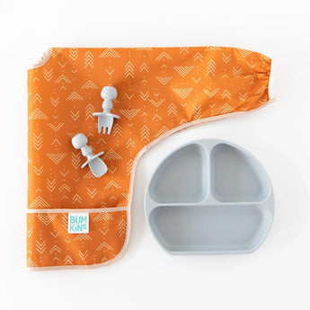 Bumkins Sleeved Bib: Grounded lays folded on a white background with gray toddler utensils on top, and a gray divided plate nearby.