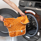 A person holds a Bumkins Sleeved Bib: Grounded in front of an open front-loading washing machine.