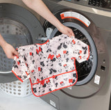 Hands placing a colorful shirt into a washer, next to a laundry basket and Bumkins Sleeved Bib: Minnie Mouse.