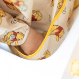 Close-up of child's hand in the front pocket of a Bumkins Sleeved Bib: Winnie Loves Hunny.