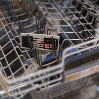 A Silicone Teether: NES™ Controller by Bumkins sits in the dishwasher, ready to soothe babys gums with nostalgic charm.
